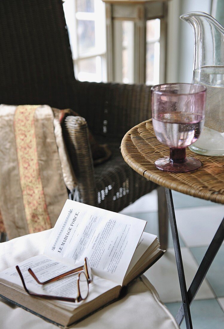 Buch und Brille auf einem Stuhl neben Tisch mit Wasserglas