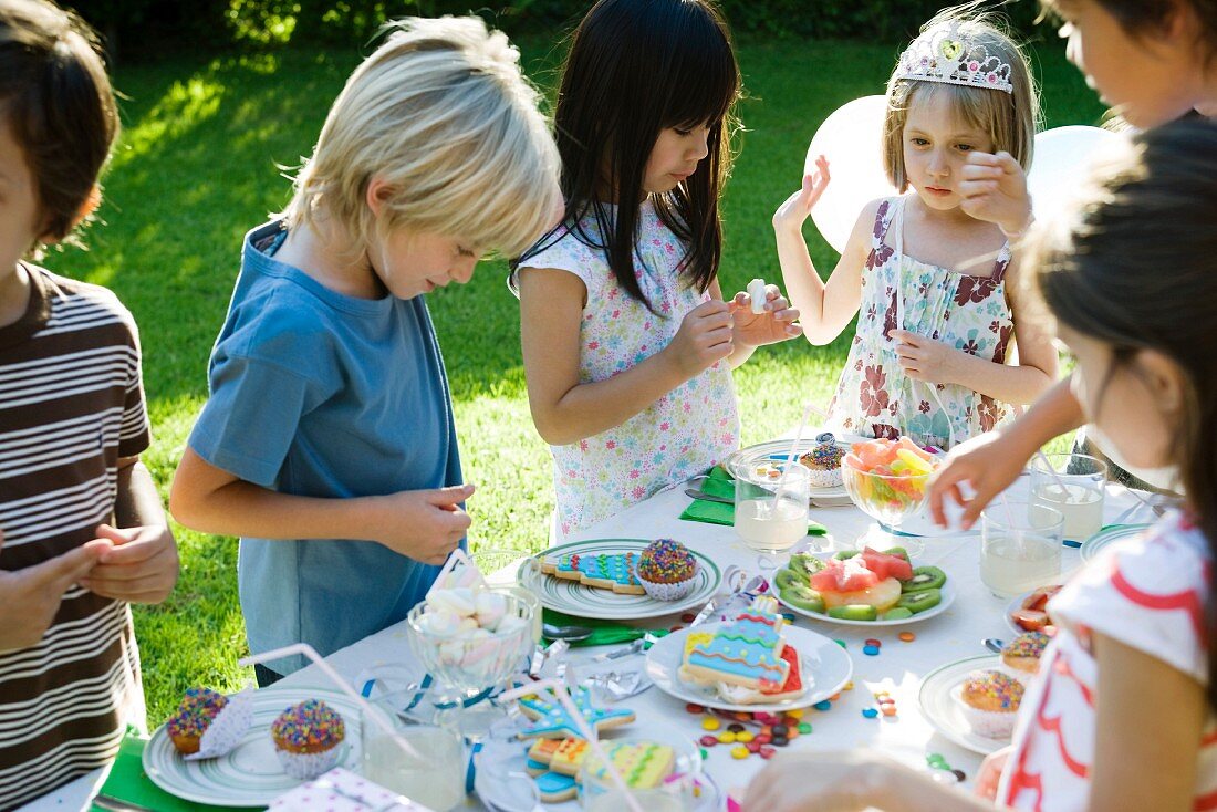 Children selecting sweets from table at outdoor birthday party