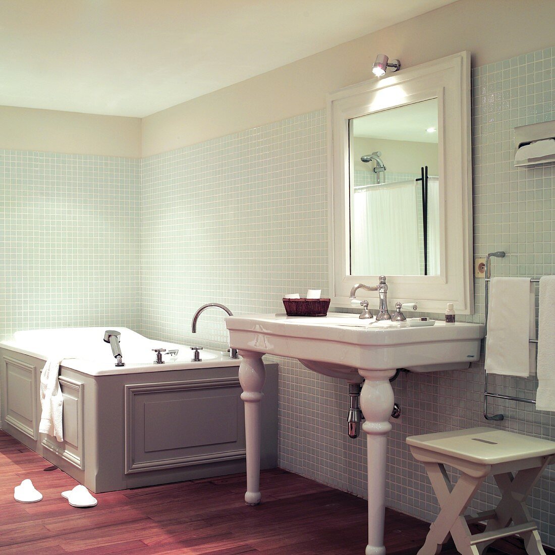 Vintage bathroom: washstand with ceramic legs next to wood-clad bathtub against mosaic-tiled walls