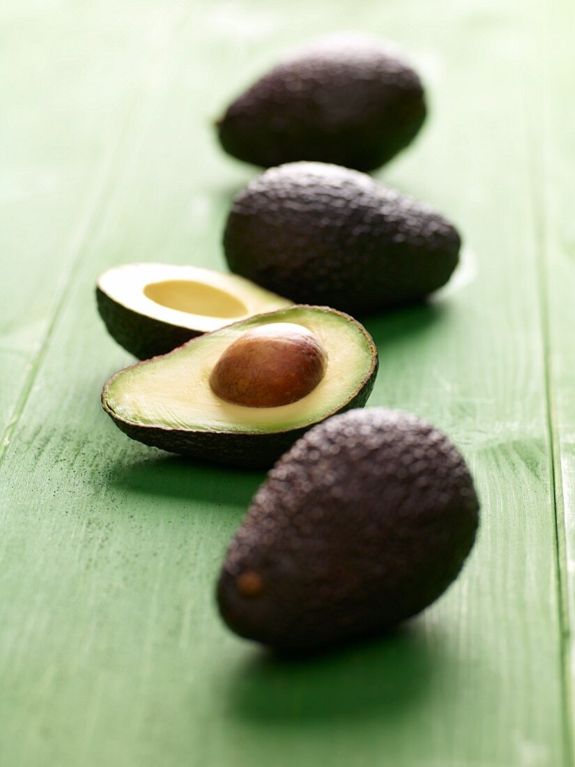 Avocados, whole and halved, on a green wooden surface