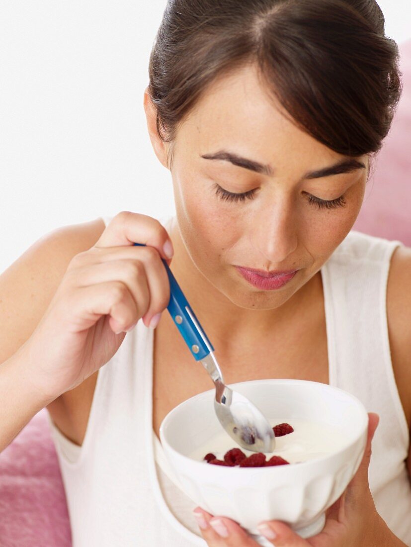 Frau isst Yoghurt mit Himbeeren