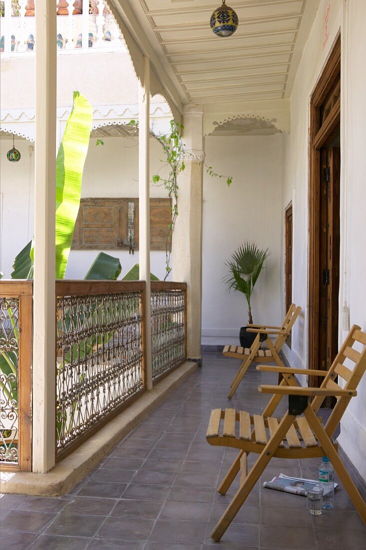 Simple wooden chairs against wall in open gallery with view into enclosed courtyard