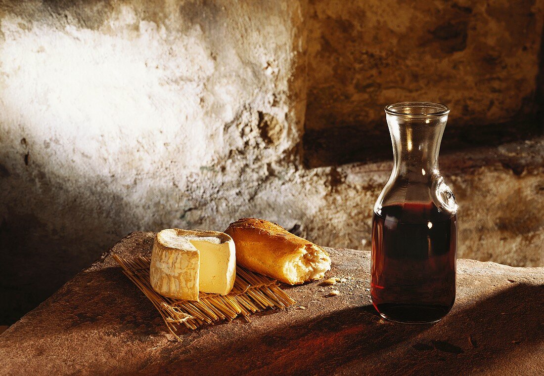 Still life: soft cheese, baguette and a carafe of red wine