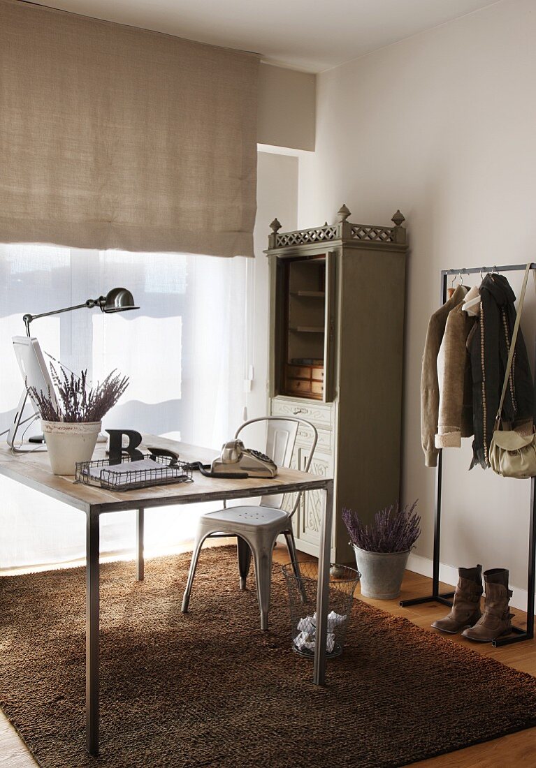 Corner of room with modern desk and vintage rustic cupboard next to window with half-closed blind