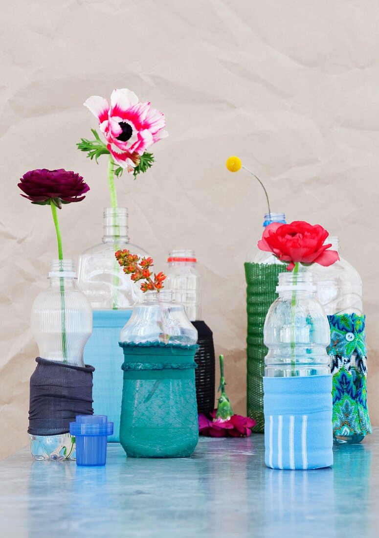 Mit Strumpfhosresten dekorierte Plastikflaschen als Blumenvasen