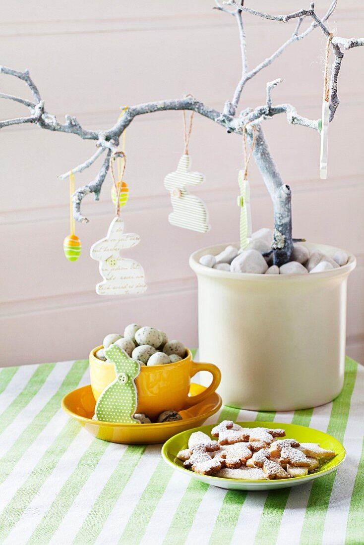 Osterbaum mit Hasen und Eiern geschmückt, darunter Tasse mit Wachteleiern und Osterplätzchen