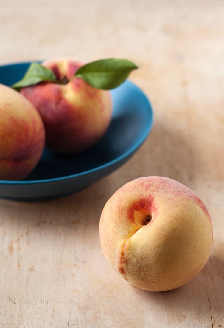 Three Fresh Peaches; Two in a Bowl; One on Wooden Board
