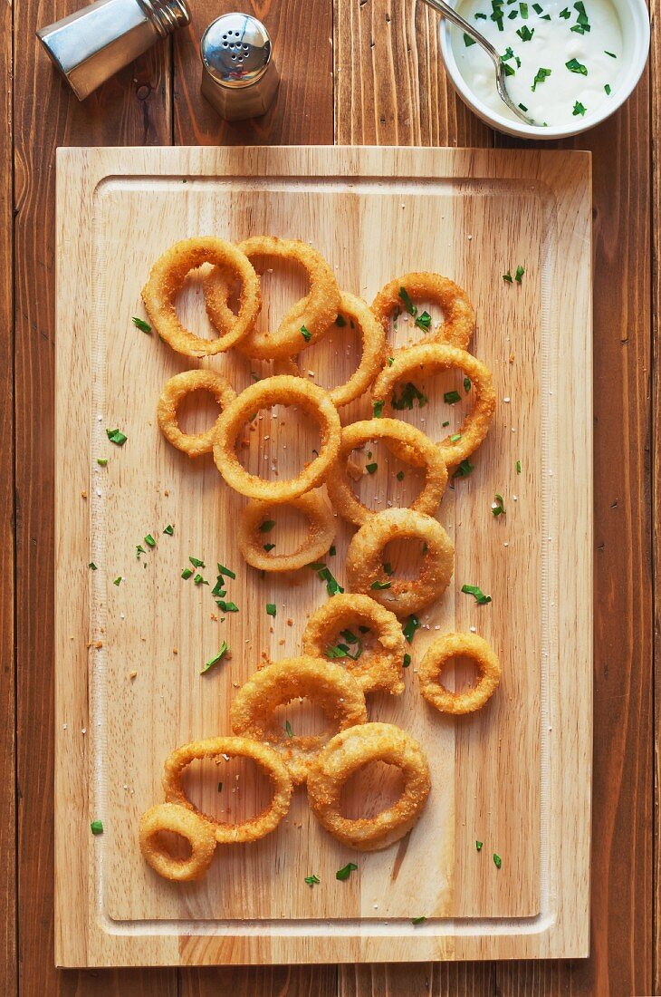 Oven Baked Onion Rings Sprinkled with Parsley and Salt on a Cutting Board; Bowl of Blue Cheese Dressing