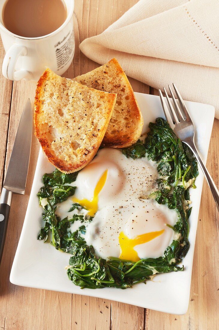 Two Fried Eggs Served Over Sauteed Spinach with Toast and Coffee