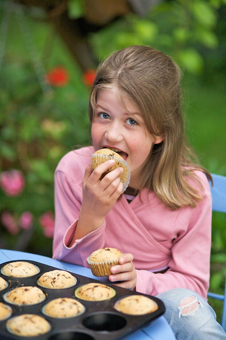 Mädchen isst Muffins am Tisch im Garten