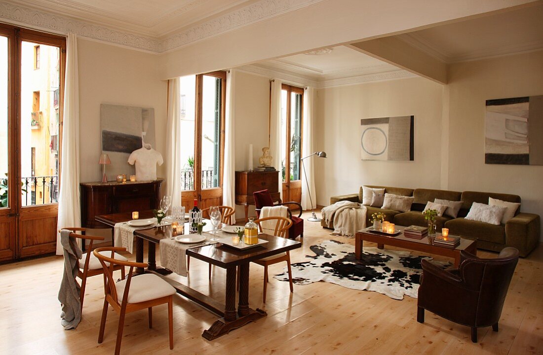 Classic wooden chairs at dining table and lounge area with cow-skin rug on wooden floor in open-plan interior