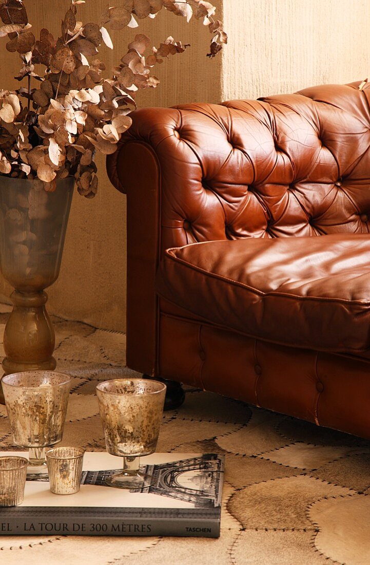 Glasses on book in front of brown quilted leather sofa with buttons; floor covering with curving, segmented pattern