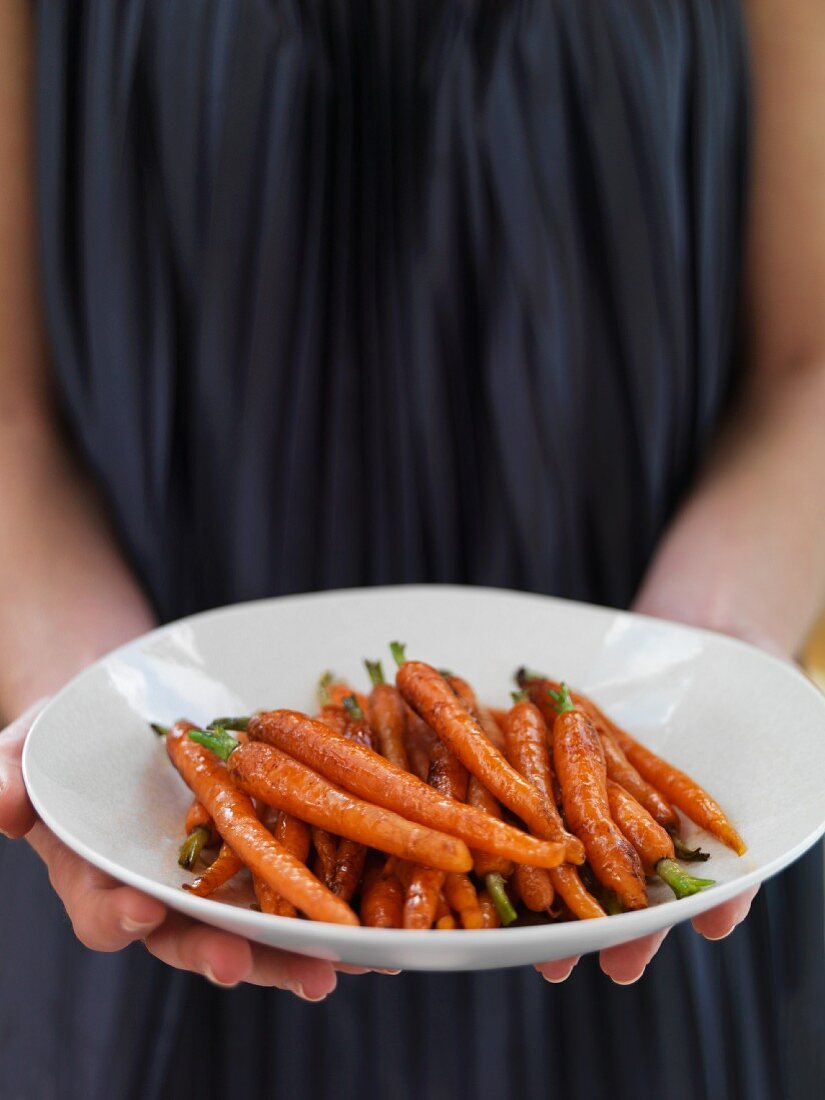A woman serving glazed carrots with balsamic vinegar