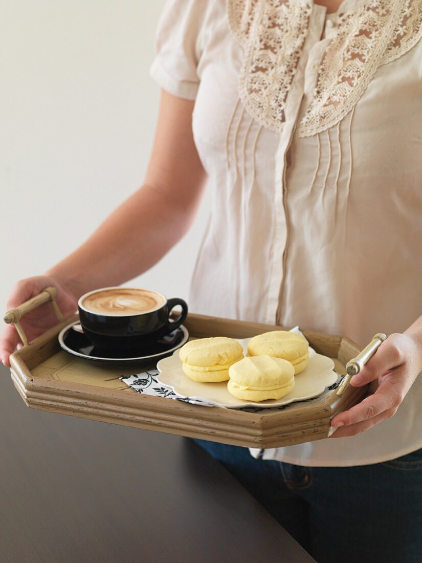 A woman holding a tray of coffee and Melting Moments