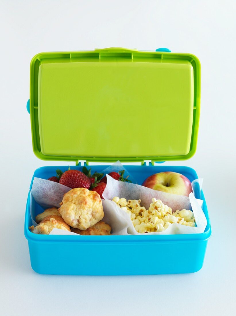 A lunch box filled with mini muffins, fruit and popcorn