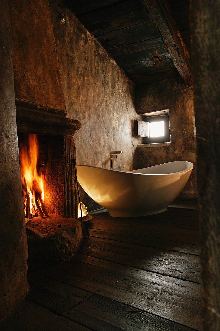 Stimmungsvolle Atmosphäre in altem Zimmer mit Kaminfeuer neben freistehender Designer Badewanne