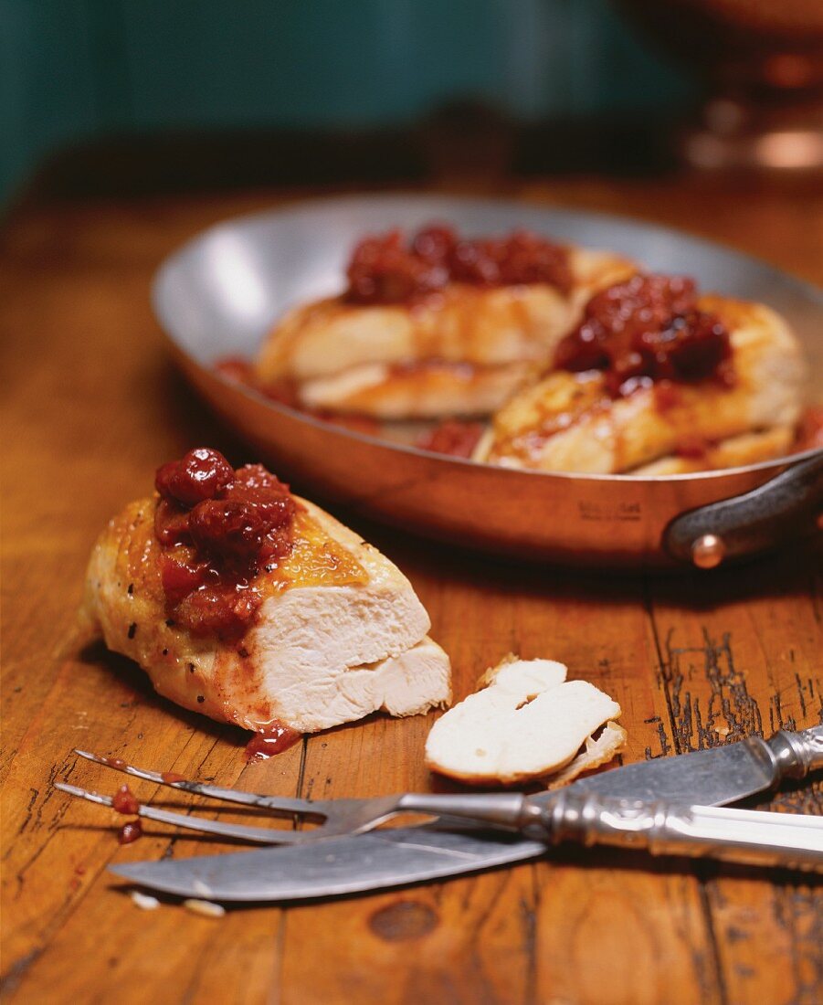 Chicken Breasts Topped with a Cherry Rhubarb Chutney; One Cut on Wooden Table; Some in Pan; Carving Set