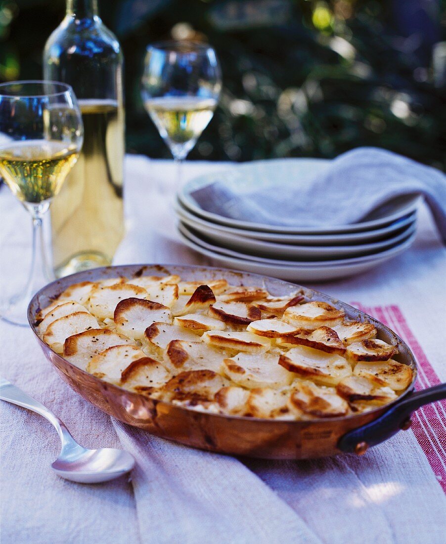 Kartoffelgratin in Kupferpfanne auf Gartentisch