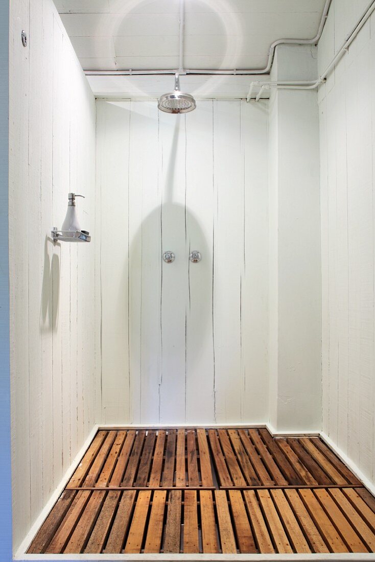 Simple shower area with white wooden walls and wooden slats on floor