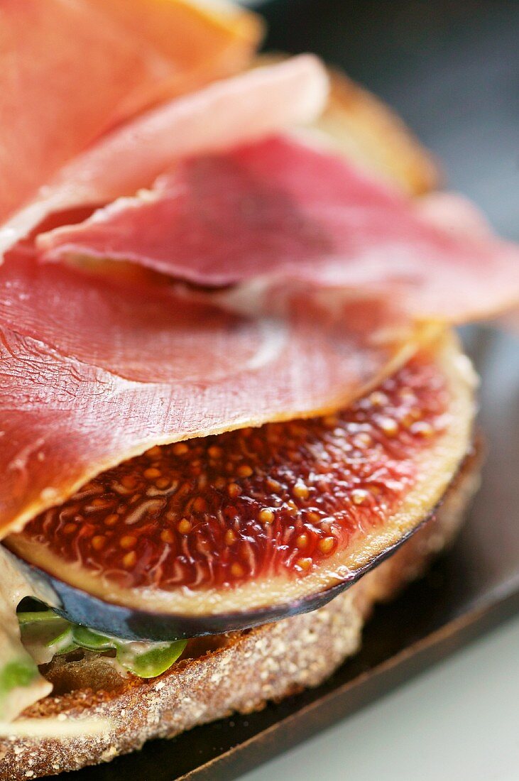 A slice of bread topped with raw ham and fresh figs (close-up)