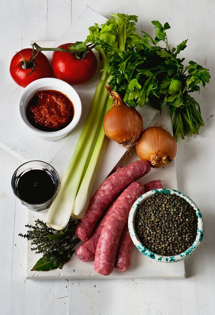 Stillleben mit Schweinswürstchen, Gemüse, Rotwein, Tomatenmark und Kräutern