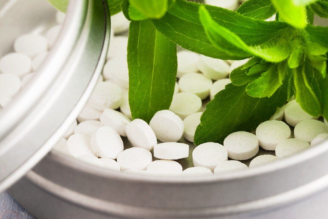 Blätter der Stevia-Pflanze und Stevia-Tabletten in kleiner Dose