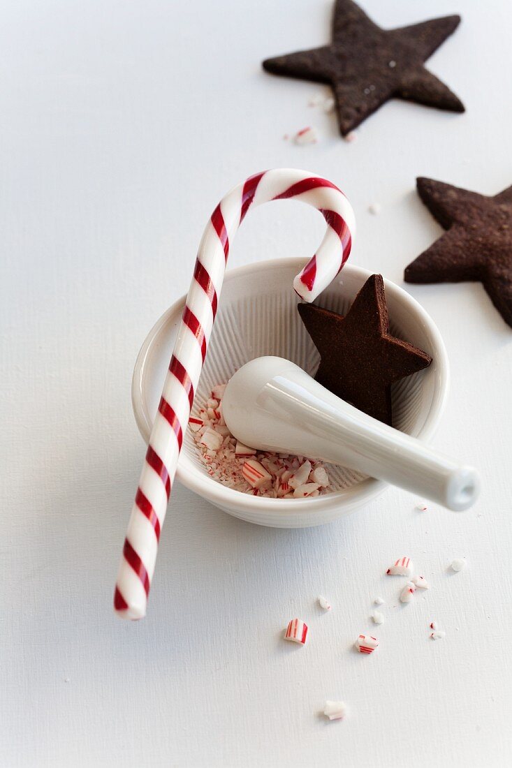 A candy cane in a mortar with chocolate star-shaped biscuits