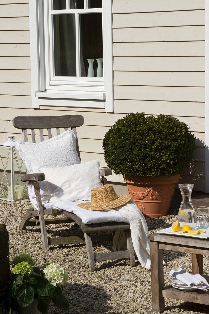 Deckchair and box bush in Tuscan planter against wood-clad facade with lattice window