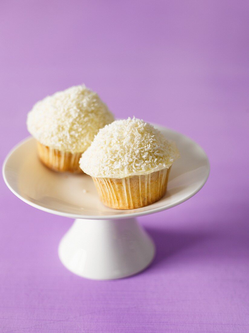 Two coconut cupcakes on a cake stand