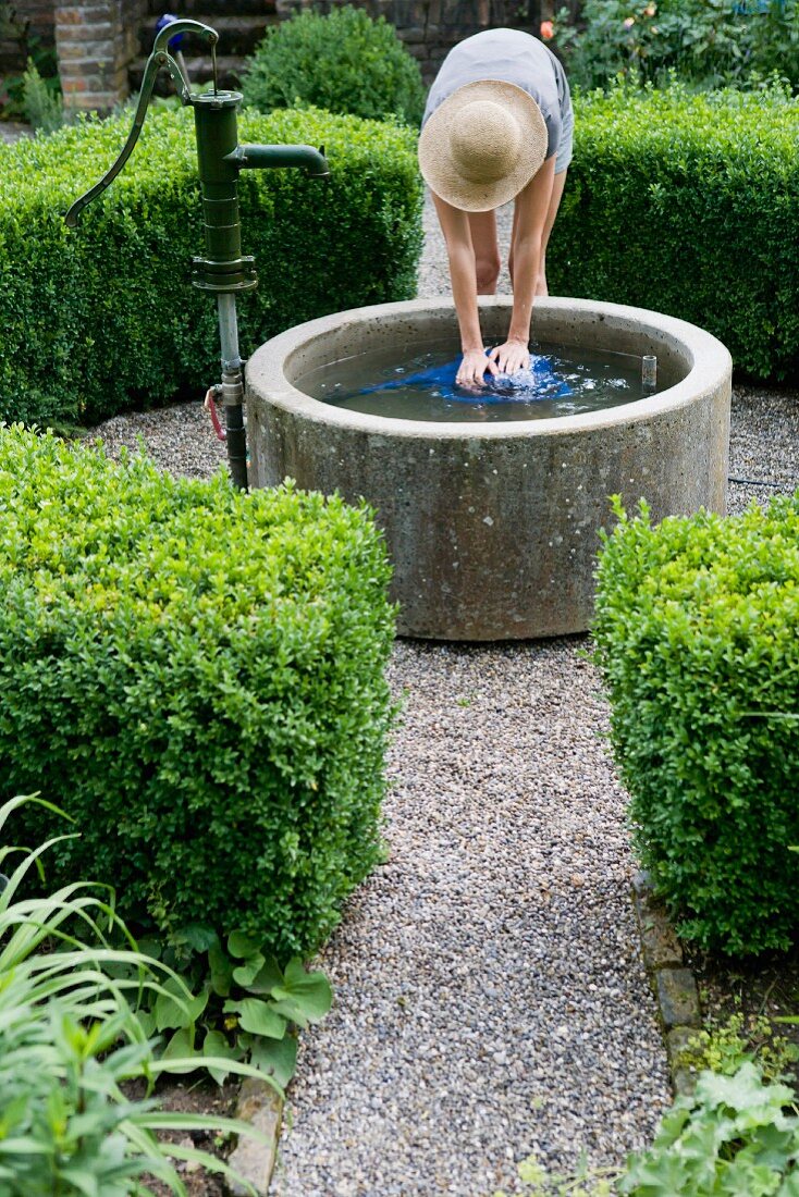 Frau füllt Giesskanne am Brunnen