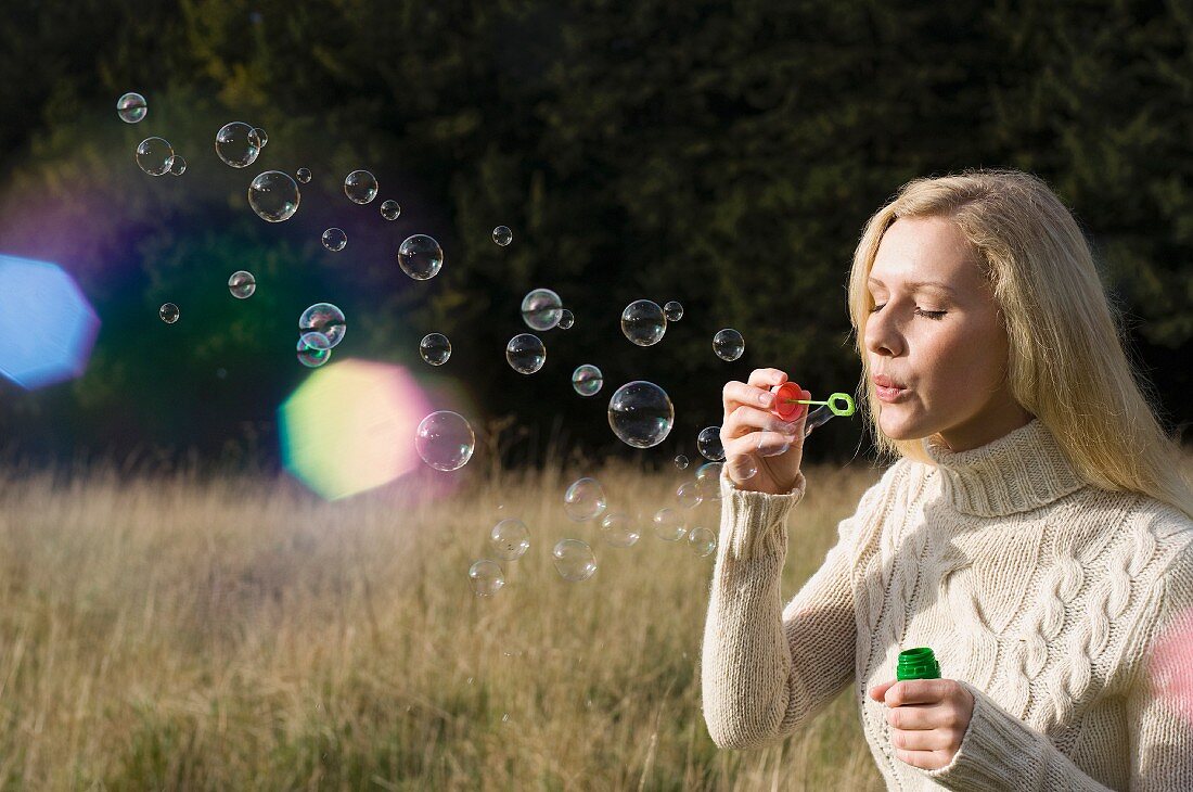 Woman blowing soap bubbles in wheat field