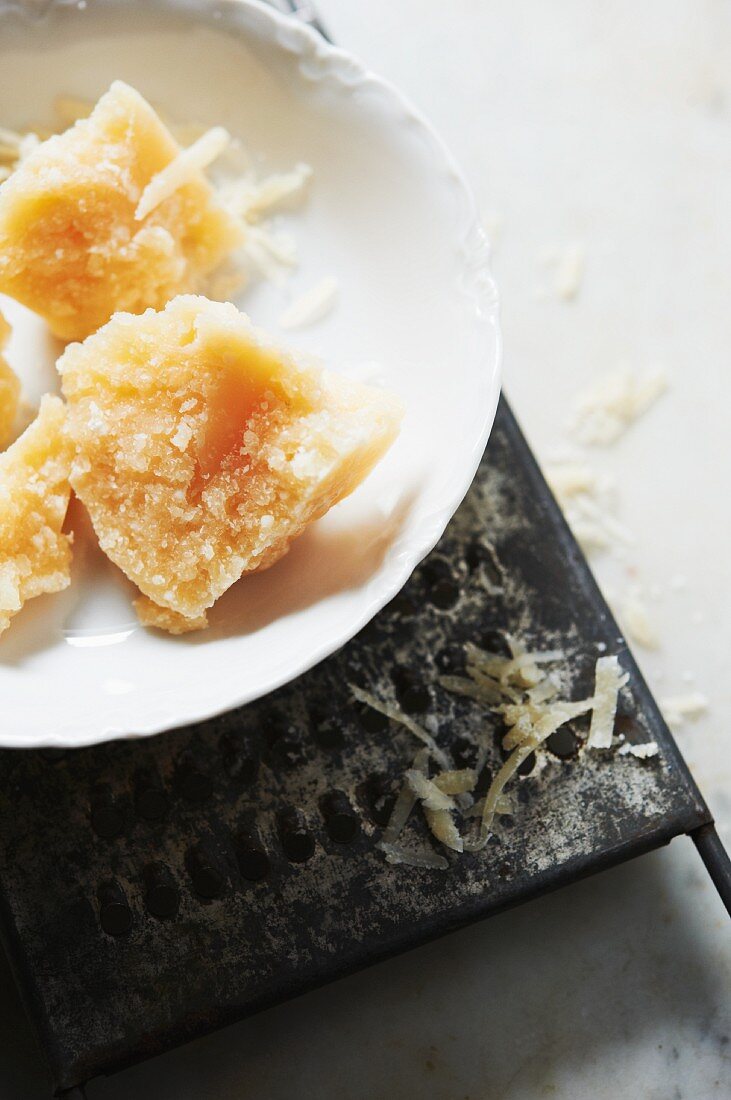 Parmigiano Reggiano in Stücken auf Teller mit Käsereibe