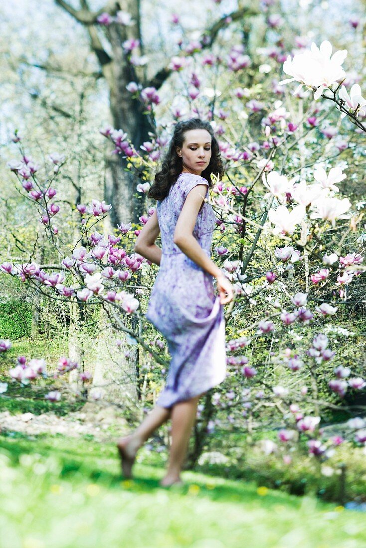 Young woman in dress walking in meadow, looking over shoulder, low angle view