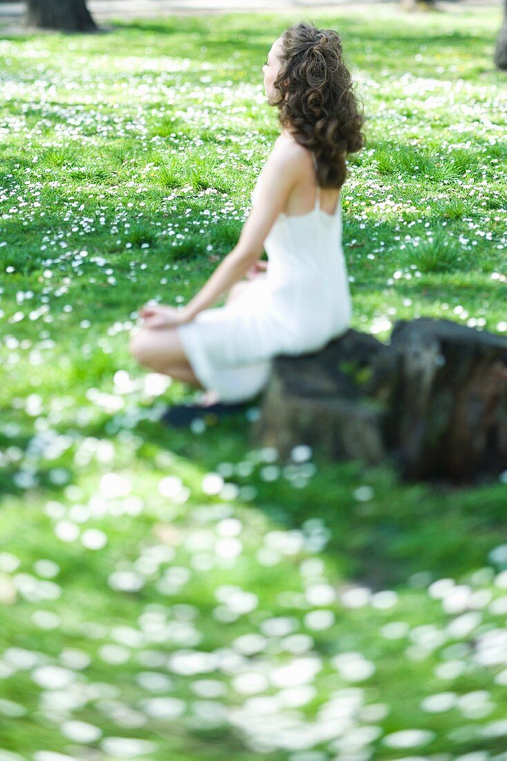 Young woman sitting in lotus position in meadow, side view, selective focus
