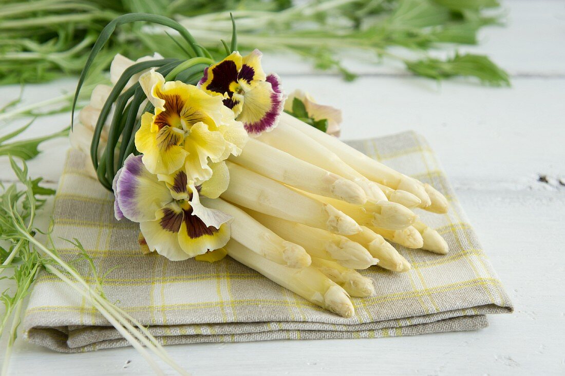 Ein Bund weisser Spargel umwickelt mit Stiefmütterchenblüten