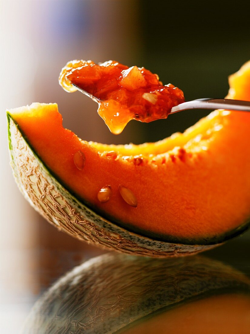 Melon and almond jam on a spoon above a slice of melon