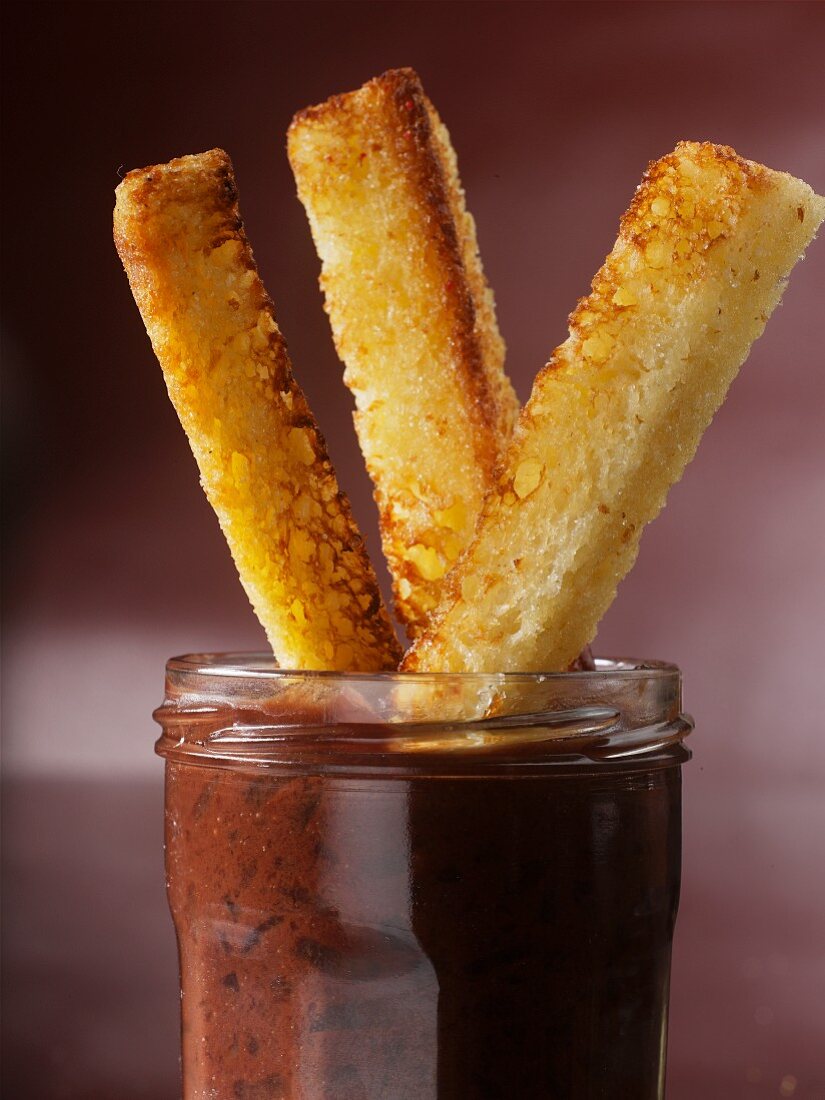 Toasted bread sticks in a jar of pear and chocolate spread