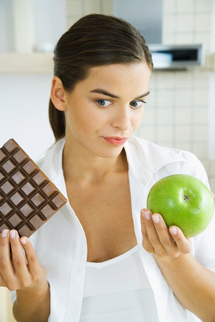 Young woman holding apple in one hand and large bar of chocolate in the other