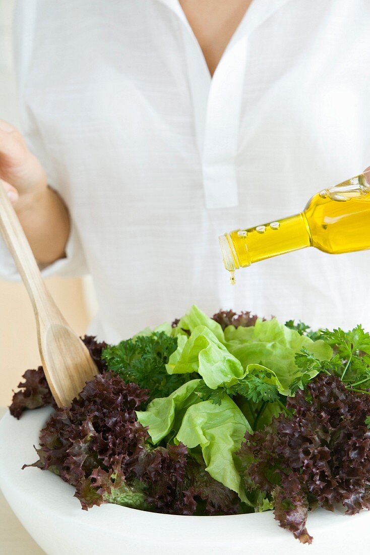 Frau träufelt Olivenöl auf Blattsalat