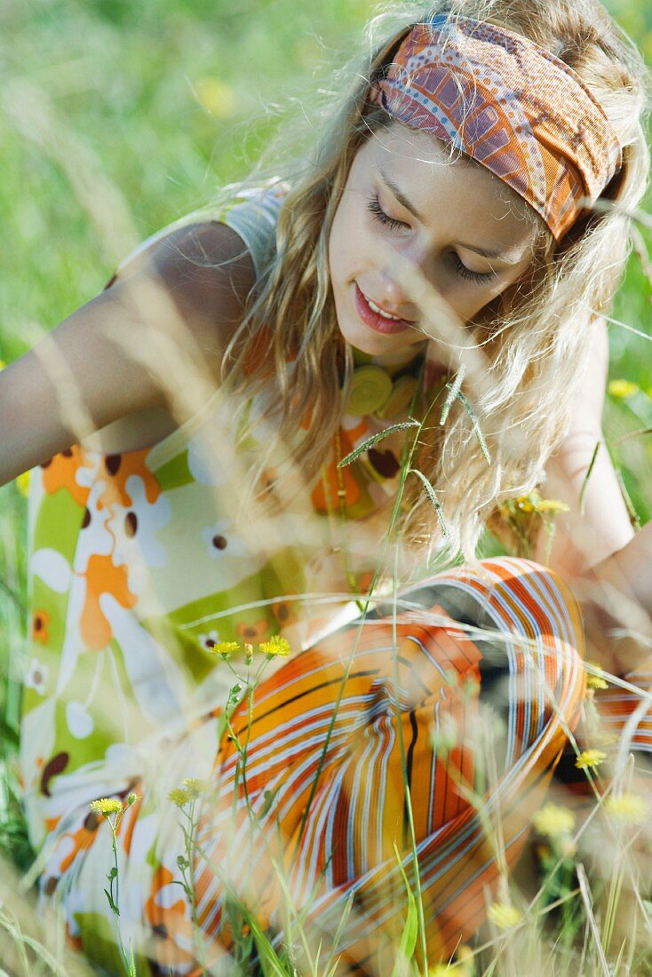 Young woman sitting in field of flowers, looking down, cropped view