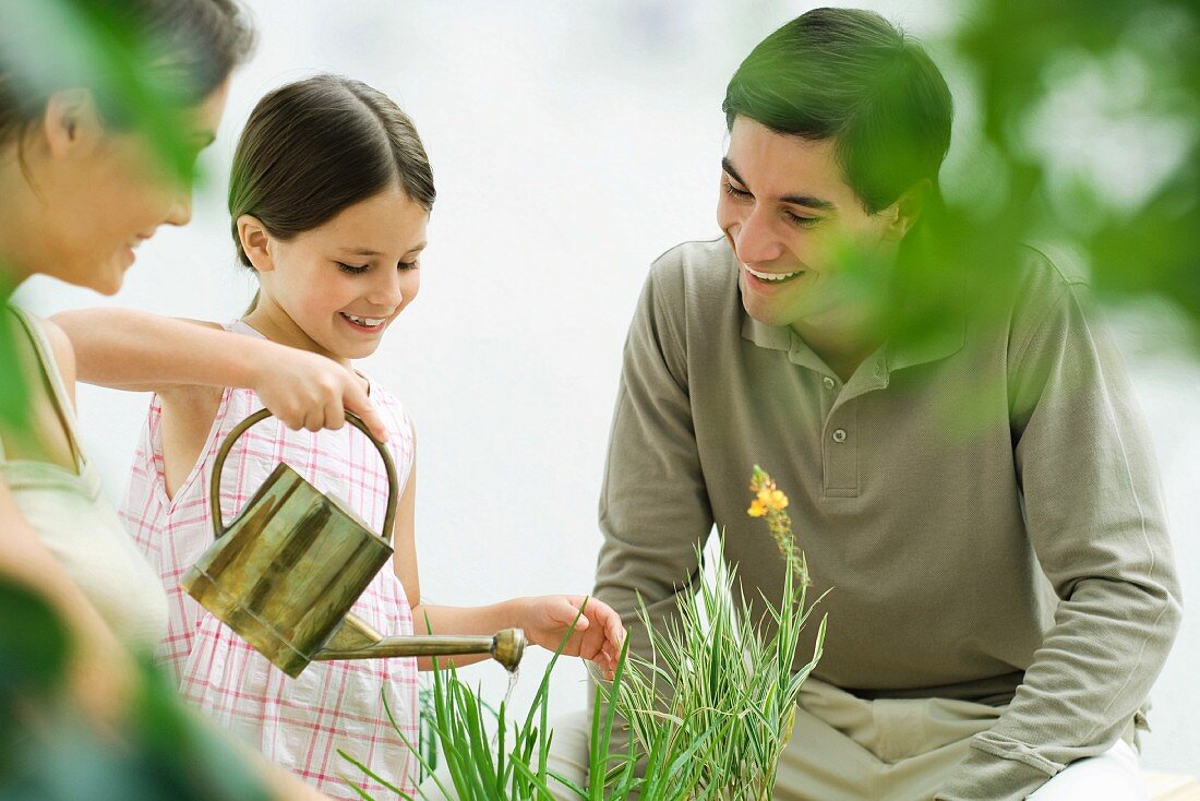 Girl watering plants, parents watching, all smiling
