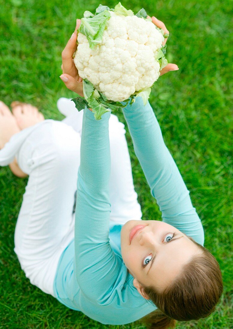 Junge Frau auf der Wiese hält Blumenkohl