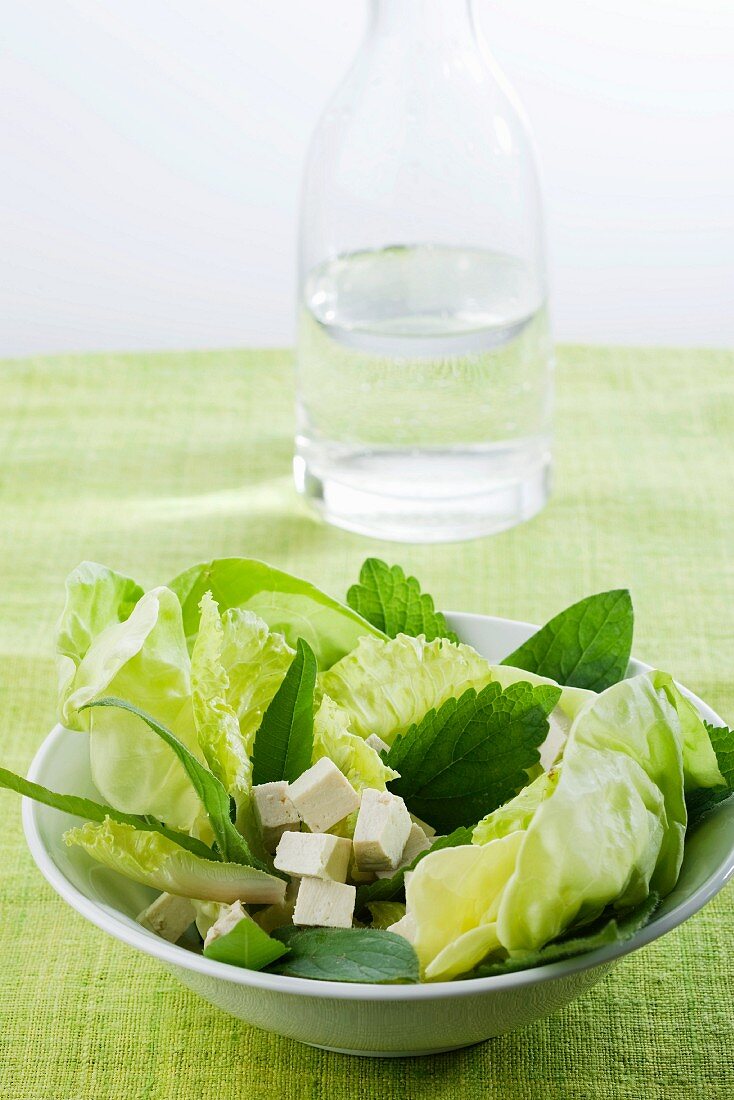 Blattsalat mit Tofuwürfeln vor Wasserkaraffe
