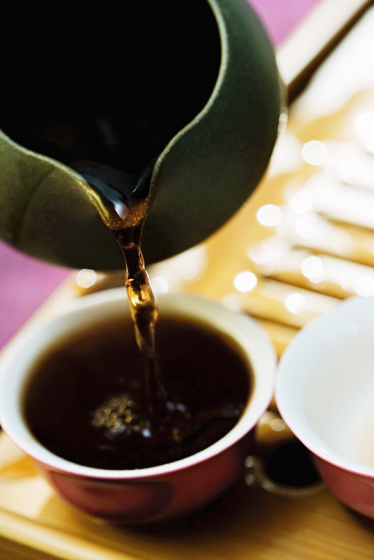 Black tea poured from teapot into cup on bamboo tea tray