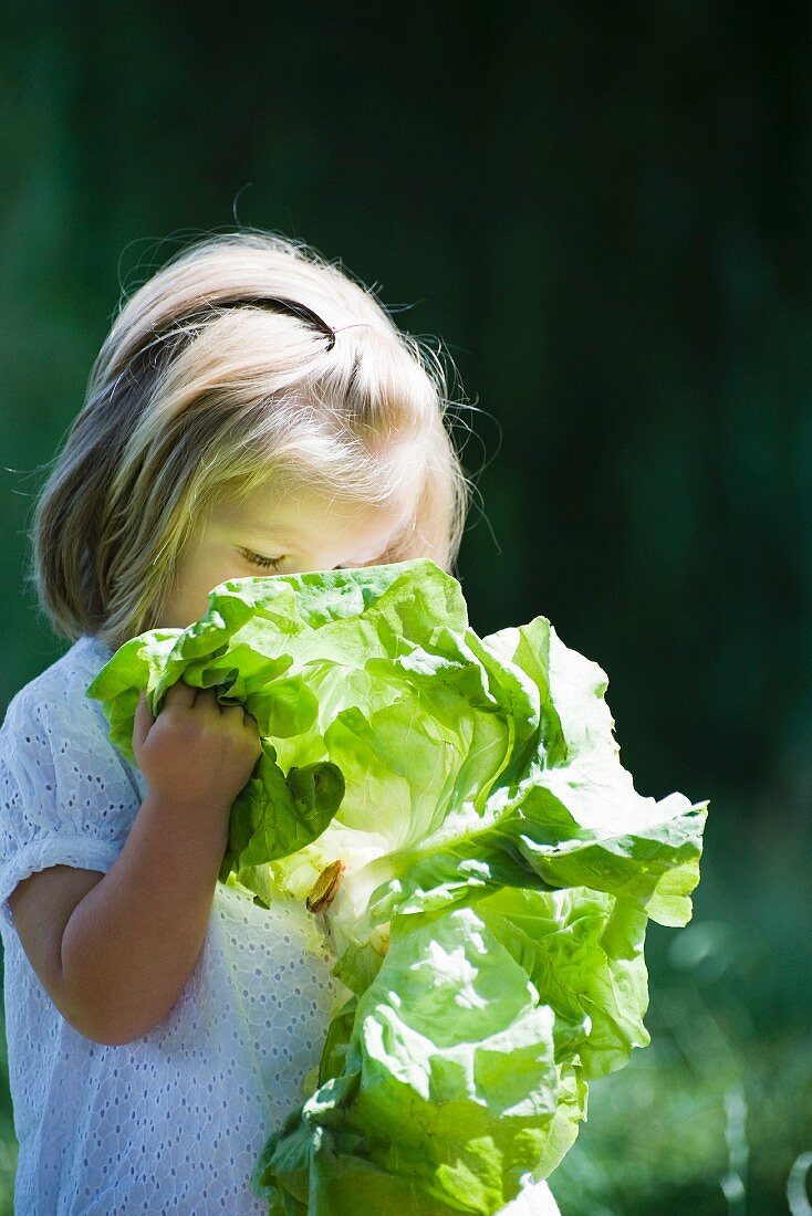 Little girl holding up chard to her face