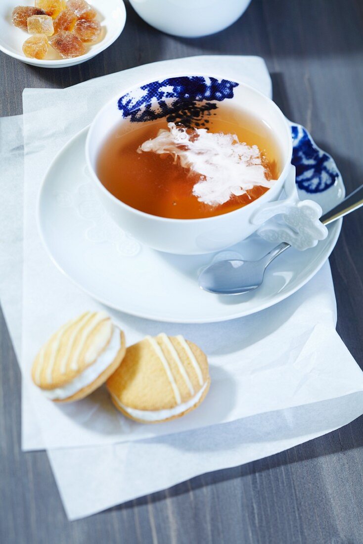 Teetasse mit Schwarzem Tee und Sahne, Kandiszucker und Keksen