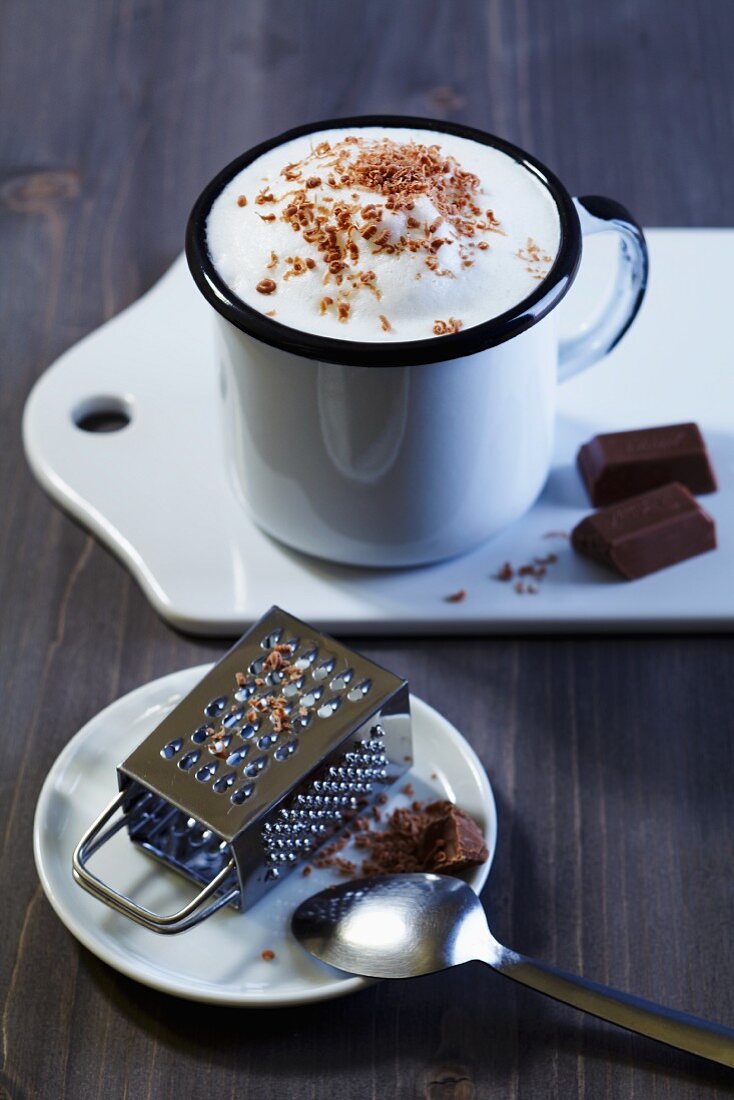 A cafe latte with milk foam and grated chocolate with a mini grater