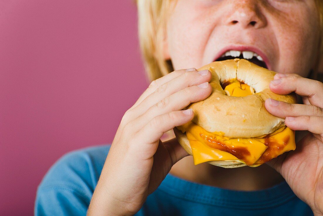 Boy eating bagel and cheese sandwich, cropped