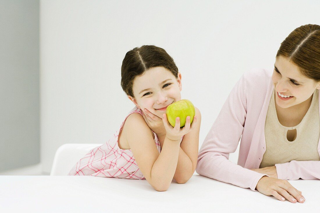 Mädchen mit Apfel neben Mutter beim Tisch
