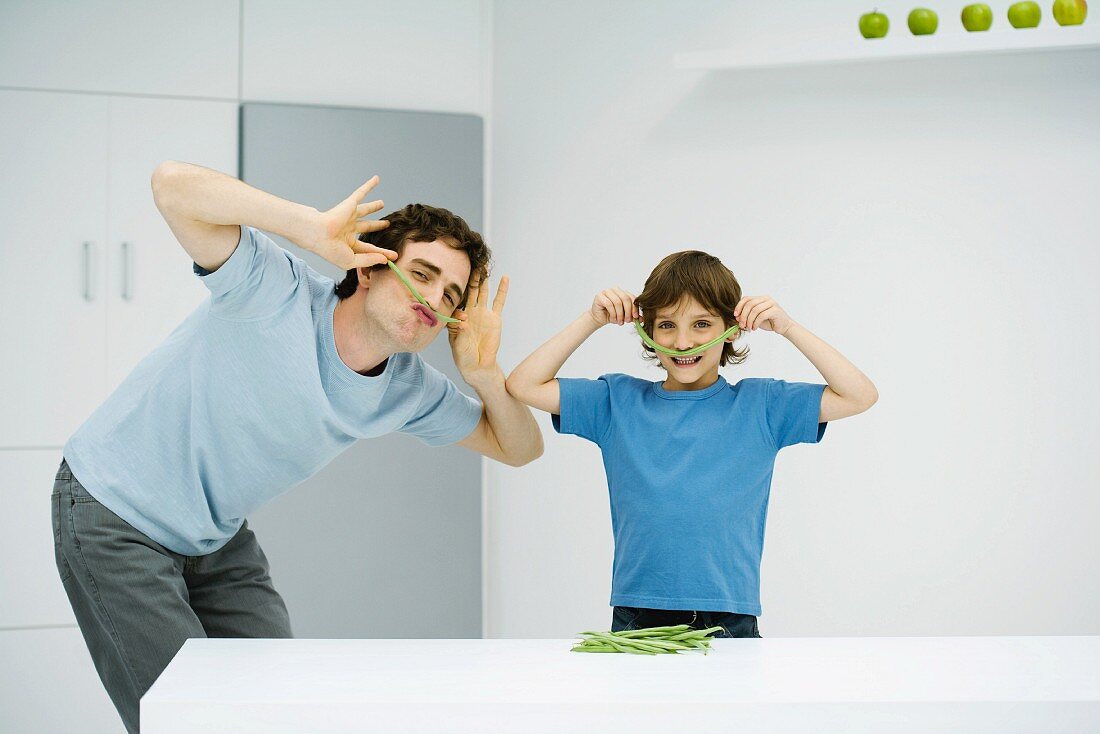 Man and boy in kitchen playing with food, smiling at camera